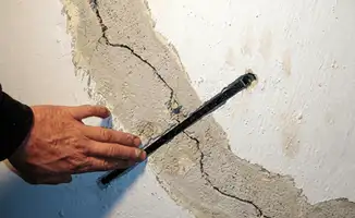 A wall with a large crack is being inspected by a professional in Mobile, AL